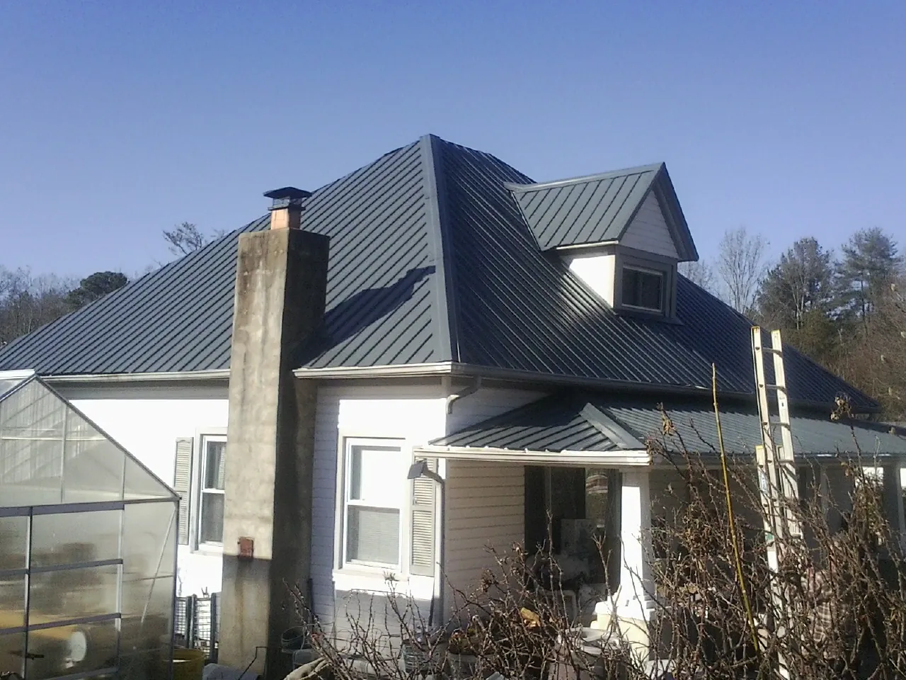 Dark blue standing seam metal roof on a white farmhouse with dormer — Slate & Tile Roof Repair by Roofing Brothers in Oklee