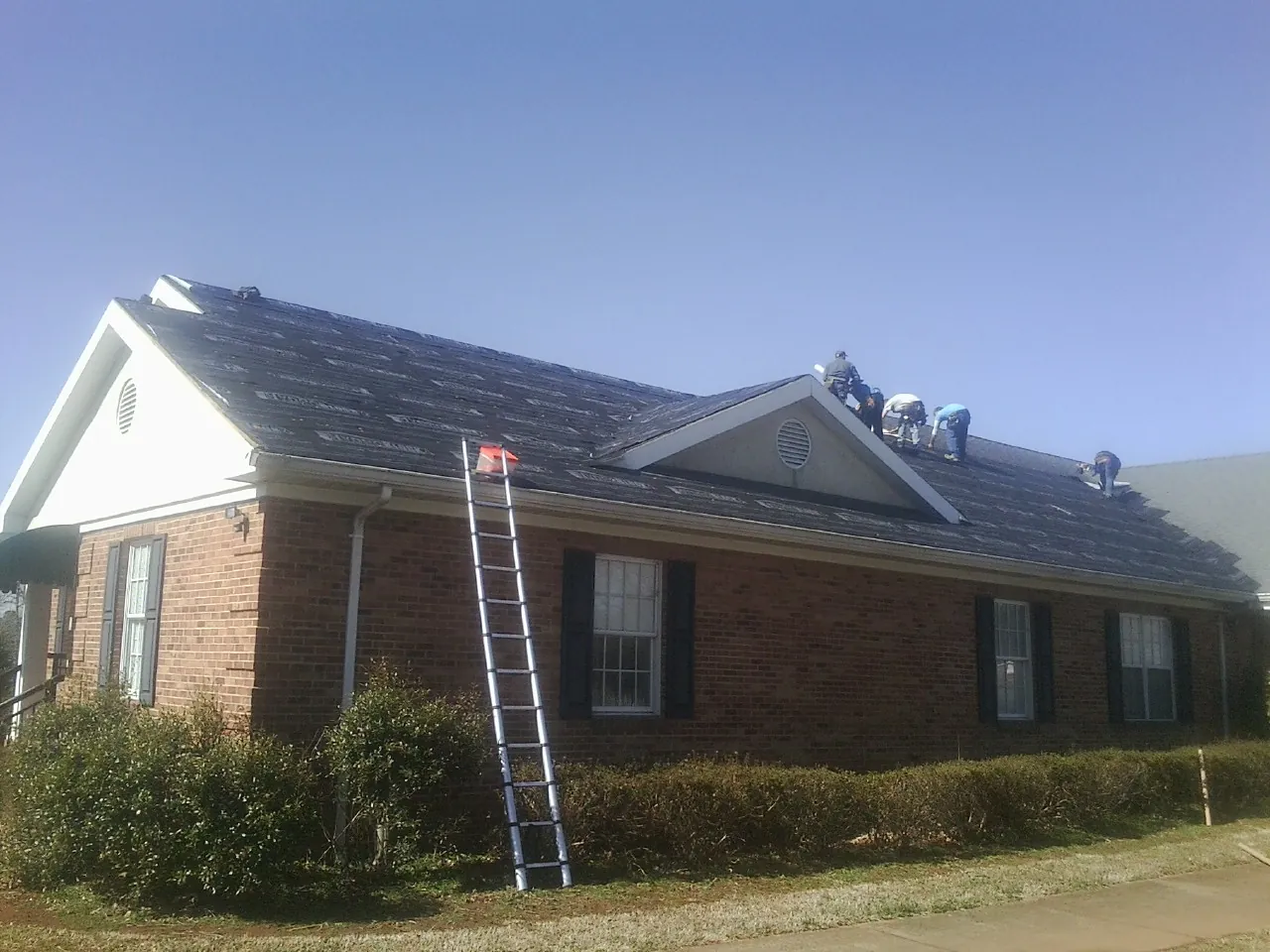 Crew tearing shingles off a brick ranch roof with a ladder set — Emergency Roof Repair work by our crew in Oklee