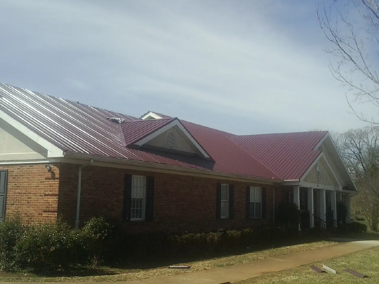 Red metal roof with gabled entries on a long brick building, from a Hail Damage Roof Repair job in Oklee
