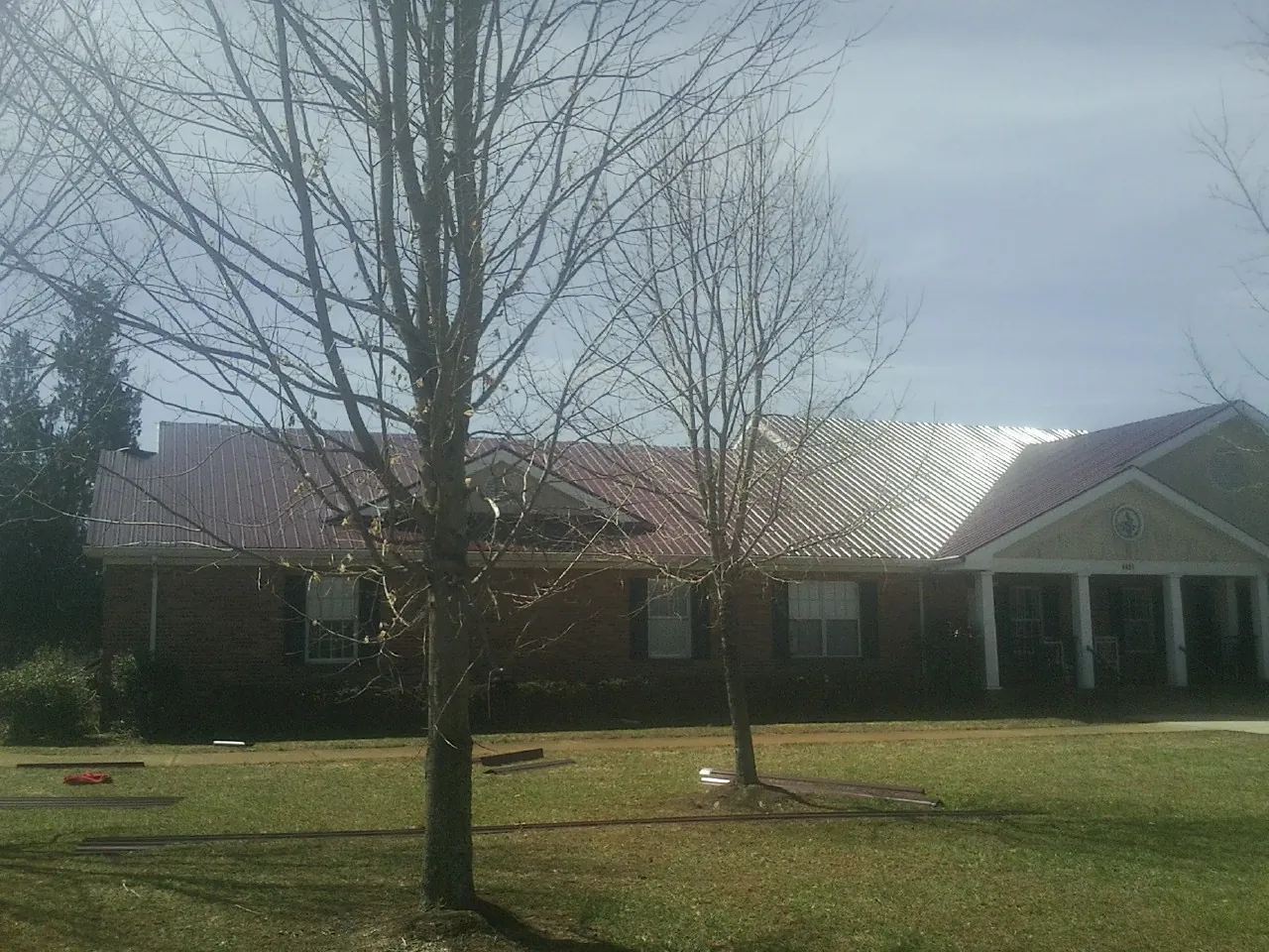 Red metal roof on a brick building seen from the front lawn in Oklee