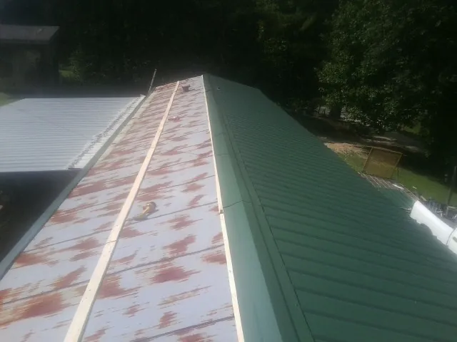 Old rusted panels beside newly installed green metal roofing — Wind Damage Roof Repair by Roofing Brothers in Oklee