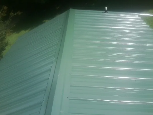New green metal panels meeting at the ridge of a roof — Flat Roof Repair work by our crew in Oklee