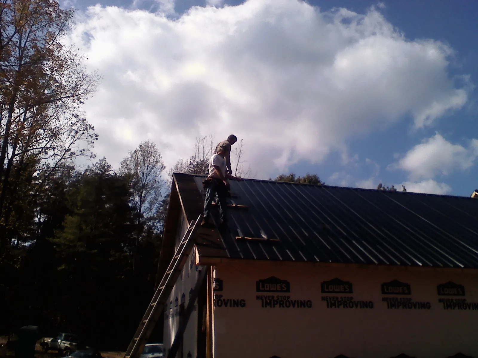 Roofer fastening dark metal panels high against a cloudy sky, from a Roof Inspection job in Oklee