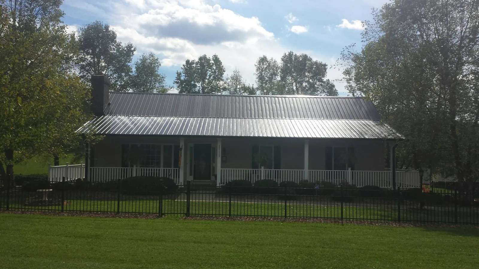 Gray metal roof on a brick ranch with a full width front porch — Gutter Guard Installation work by our crew in Oklee